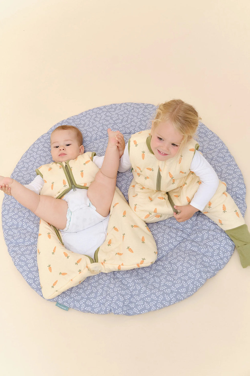 Dois irmãos a brincar num tapete, o bebé usa o saco de dormir MolisandCo TOG 2.5 [Carrots] amarelo.