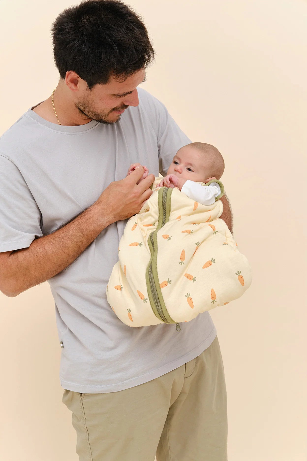 Pai a segurar um bebé no colo, que veste o saco de dormir MolisandCo TOG 2.5 [Carrots] amarelo com padrão.