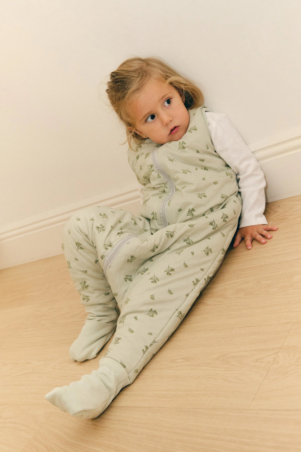 Menina sentada no chão, encostada à parede, com saco de dormir MolisandCo TOG 2.5 com pés Botany Green e meias antiderrapantes.