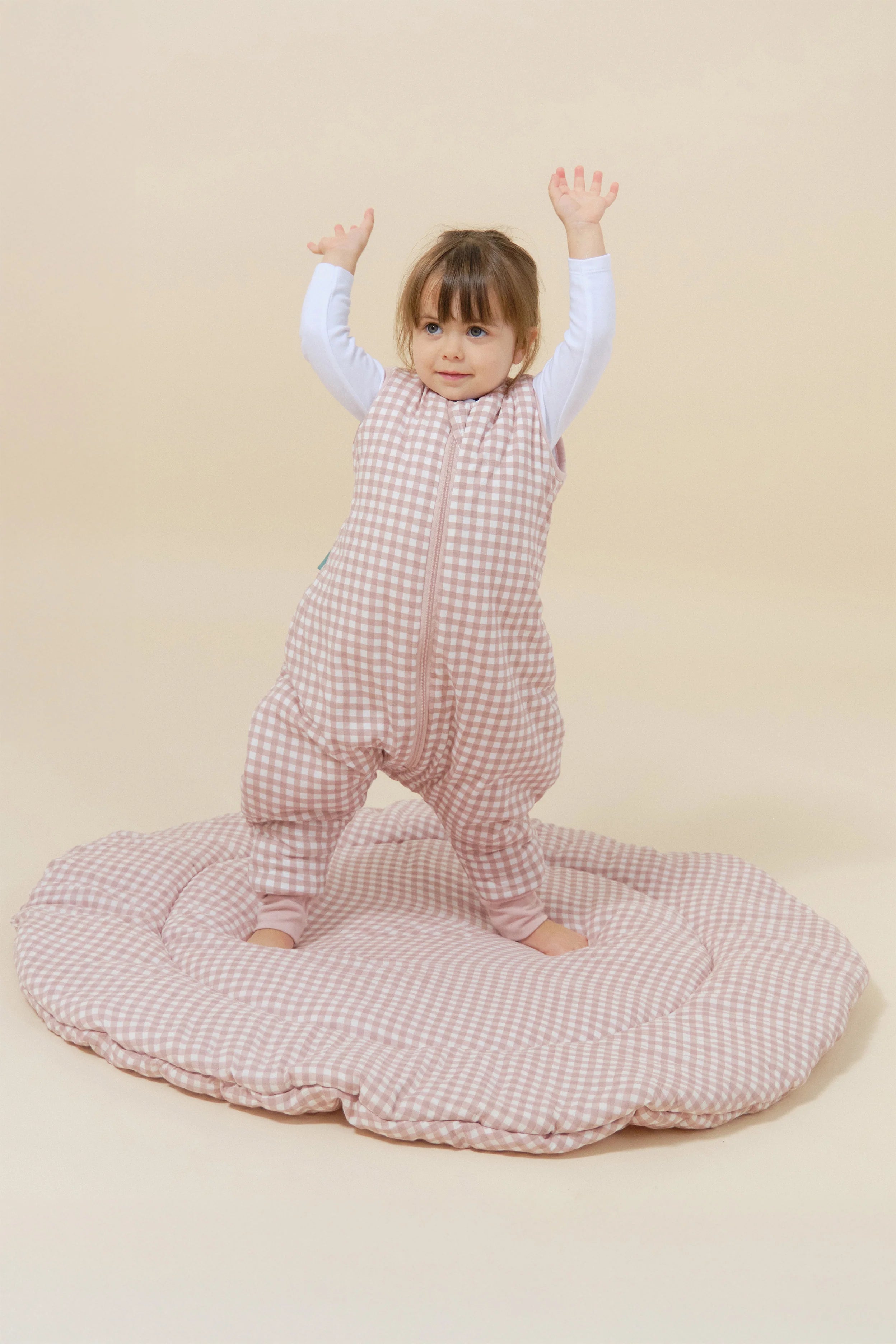 Bebé em pé, braços erguidos, sobre tapete, veste saco de dormir MolisandCo TOG 2.5 com pés rosa xadrez.
