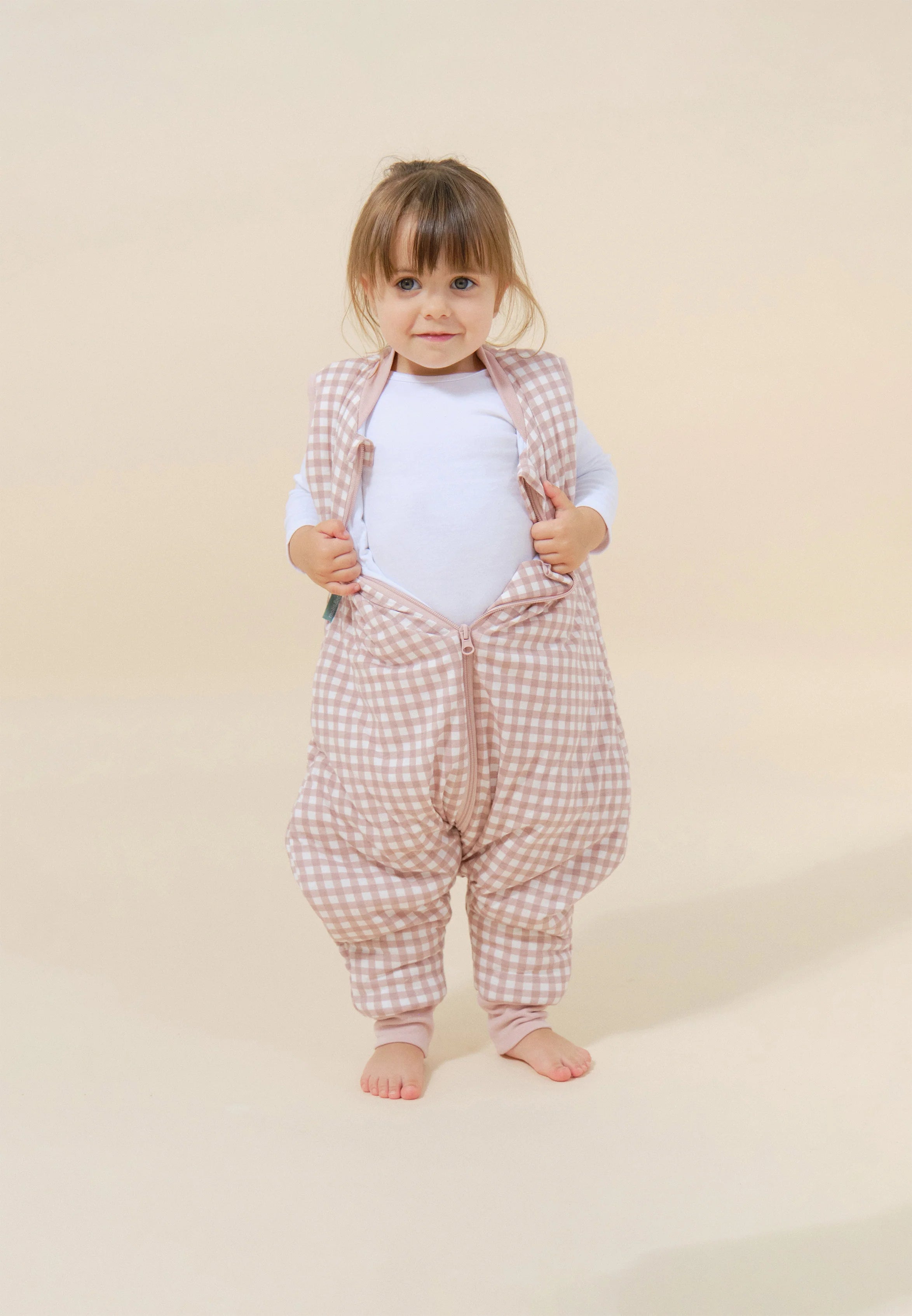 Bebé em pé com saco de dormir MolisandCo TOG 2.5 com pés rosa xadrez, a mostrar o fecho.