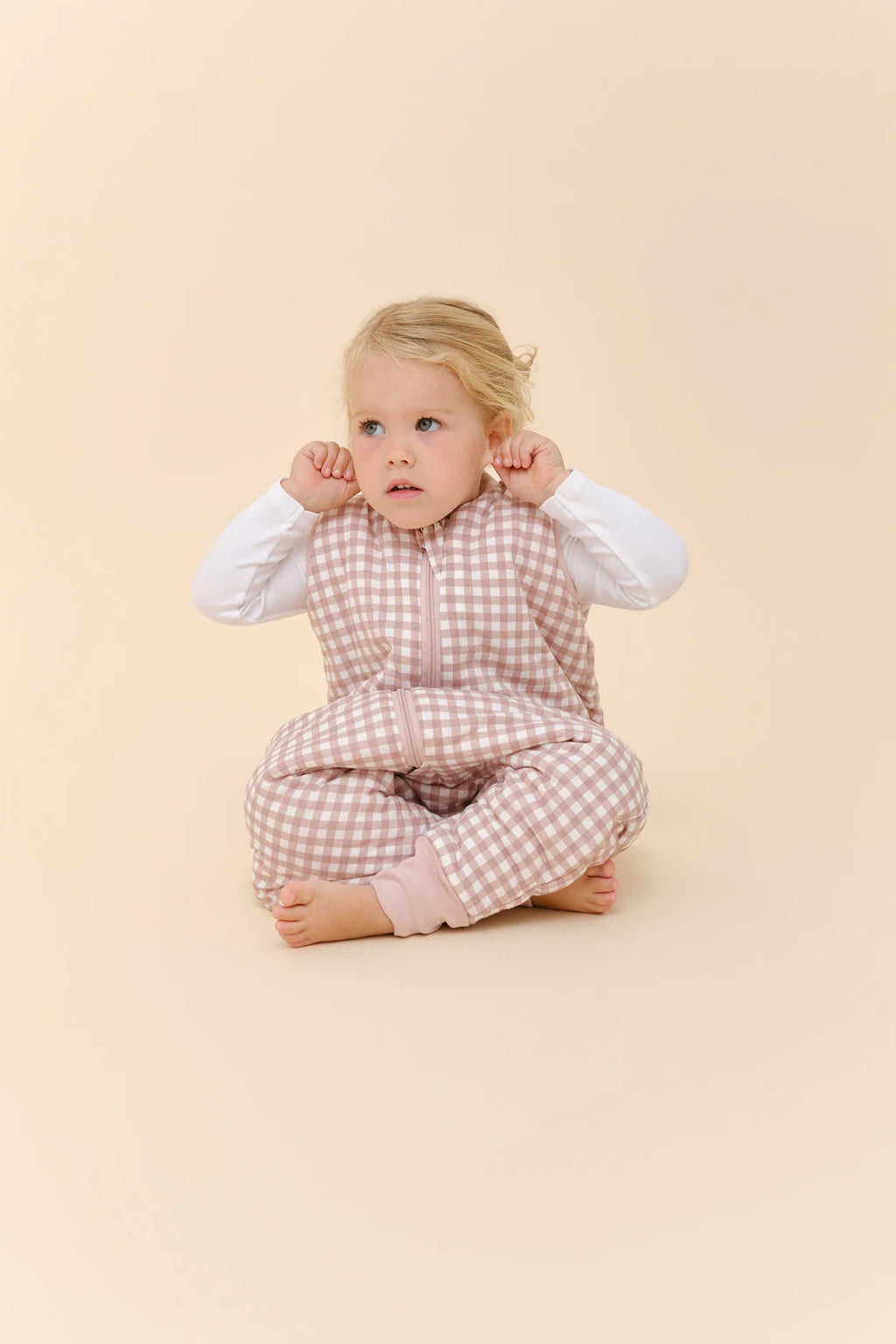 Bebé sentada com saco de dormir MolisandCo TOG 2.5 com pés rosa xadrez, a brincar.