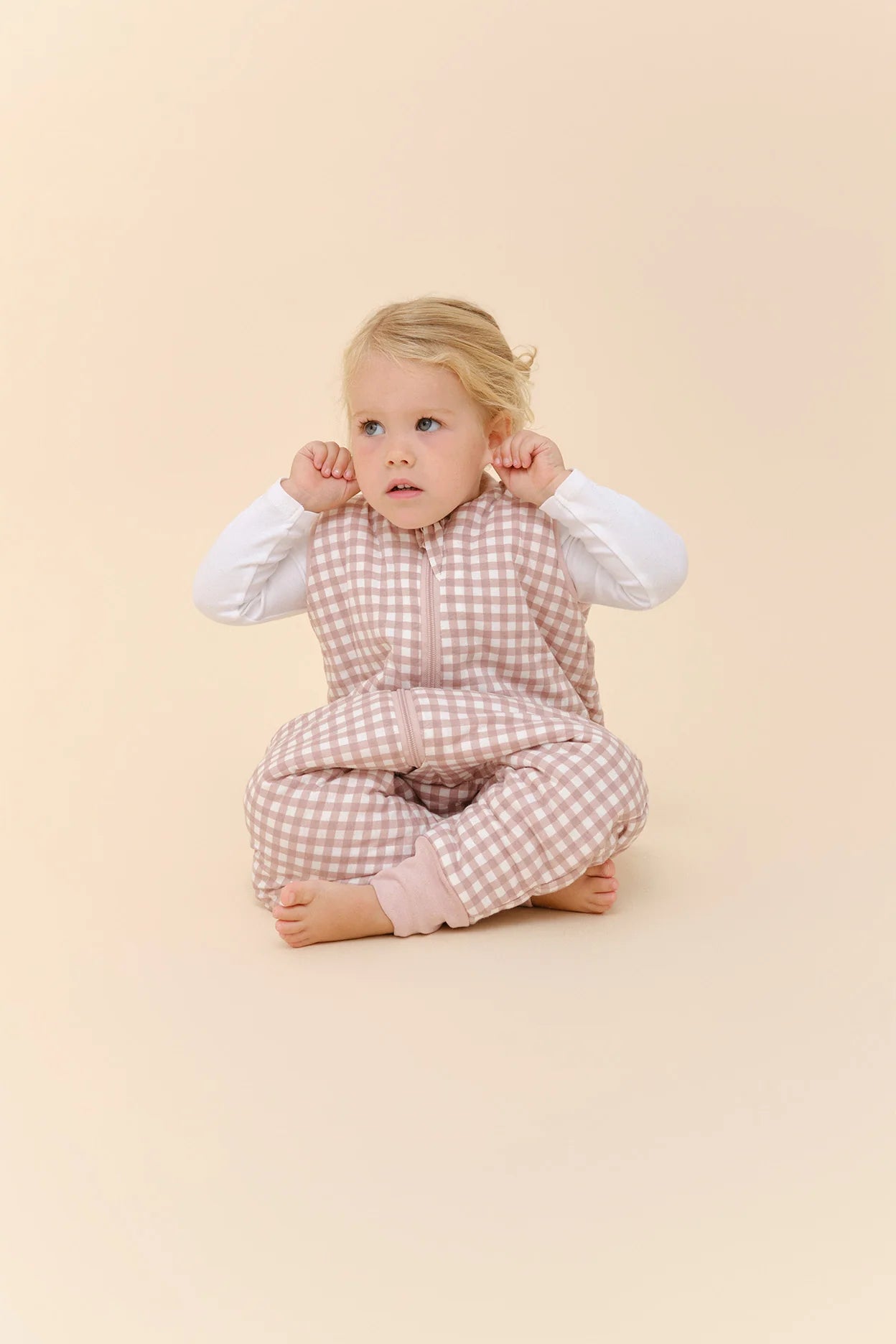 Bebé sentada com saco de dormir MolisandCo TOG 2.5 com pés rosa xadrez, a brincar.