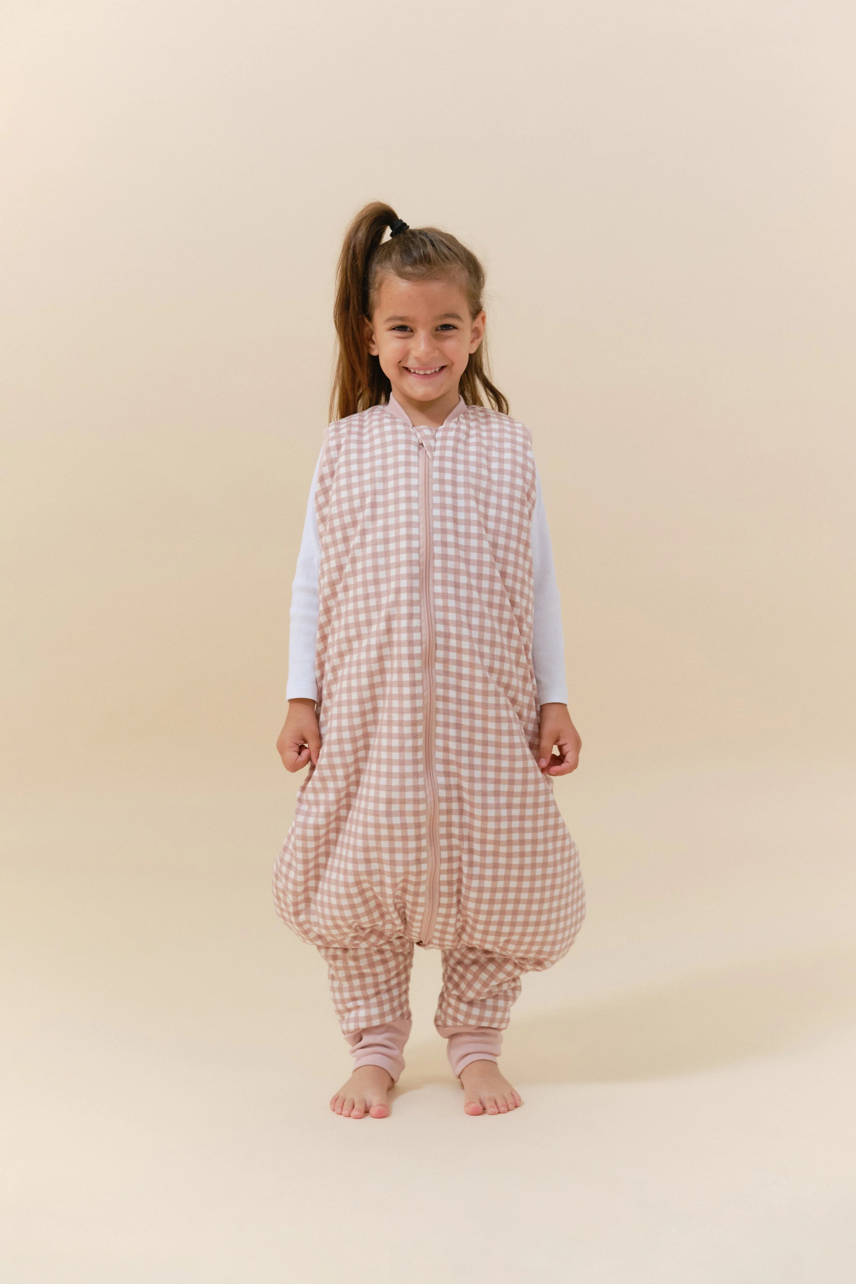 Menina sorridente veste saco de dormir MolisandCo TOG 2.5 com pés, padrão xadrez rosa. Mostra liberdade de movimento.