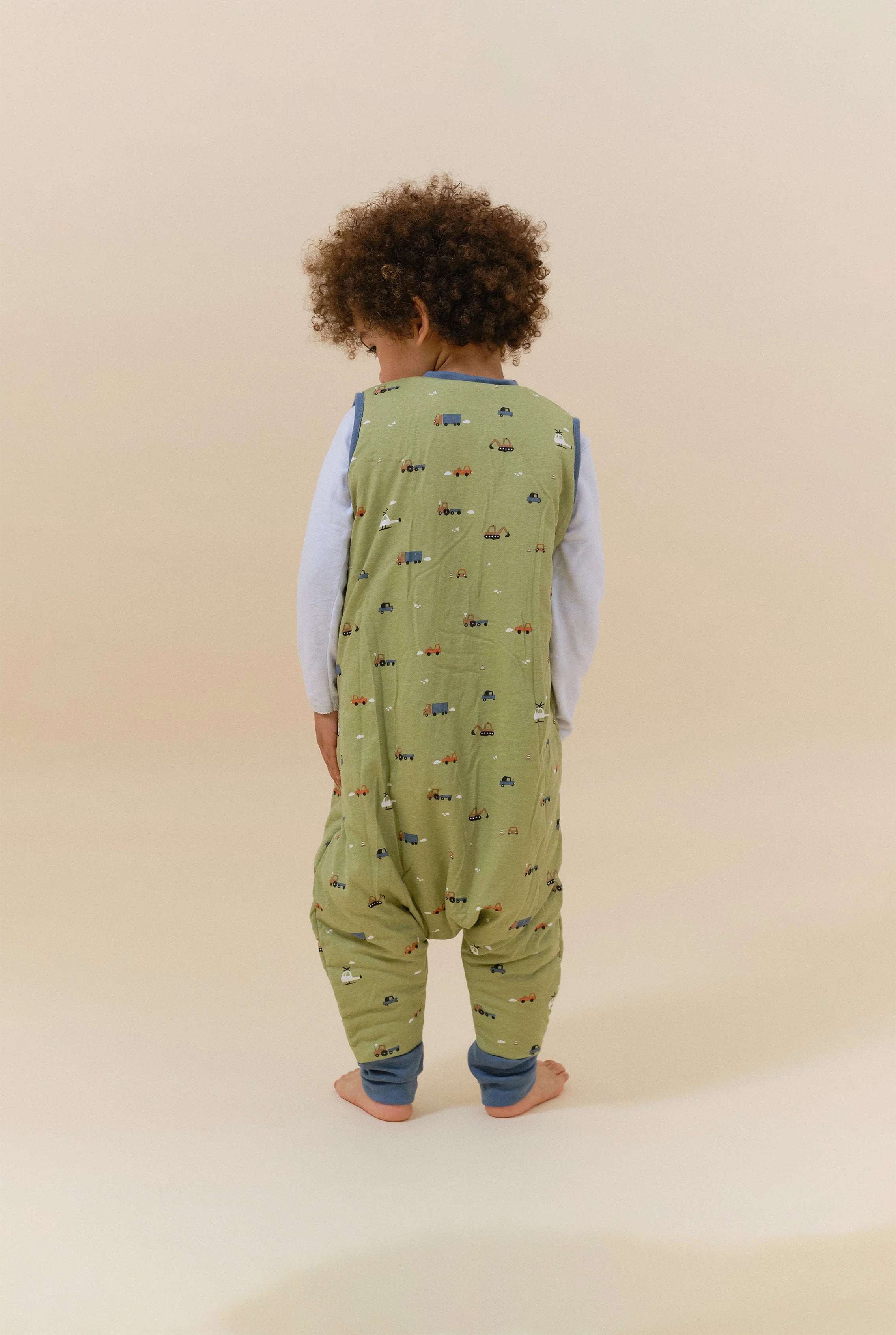 Criança de costas a usar o saco de dormir MolisandCo TOG 2.5 com pés, padrão Little Drivers, verde.