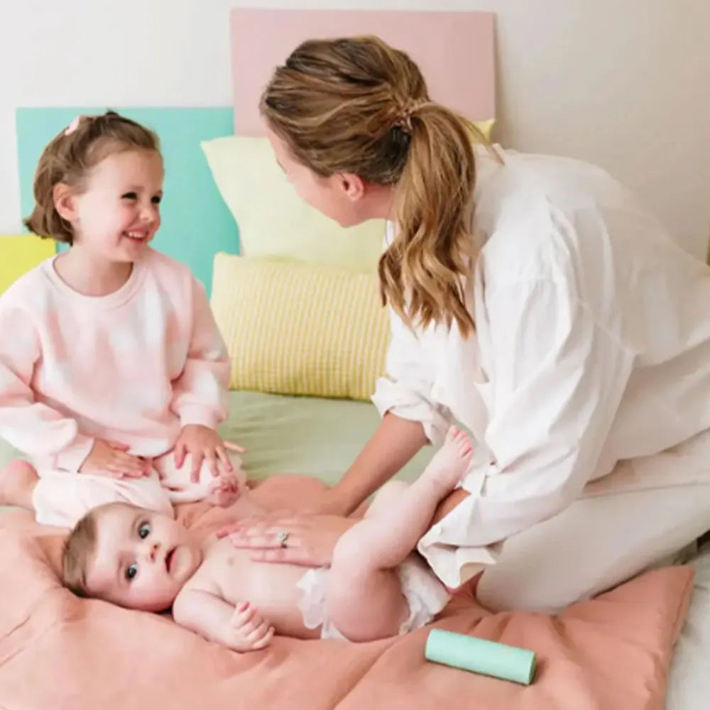 Mãe a fazer massagem a um bebé, com a filha mais velha a observar sorridente, usando o óleo Monjour.