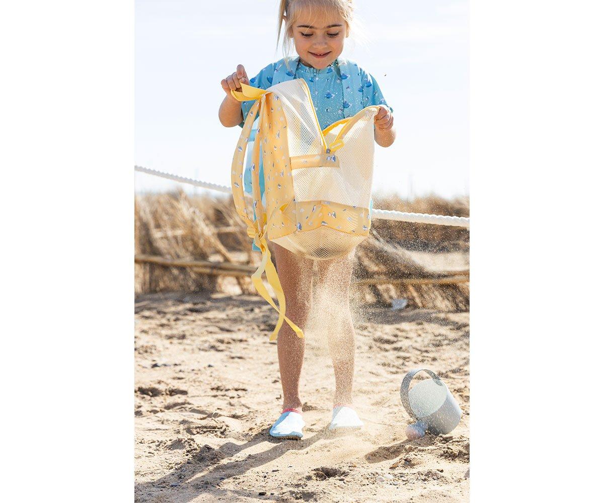 Menina a esvaziar areia da mochila de praia Monneka, mostrando a funcionalidade anti-areia e drenagem.