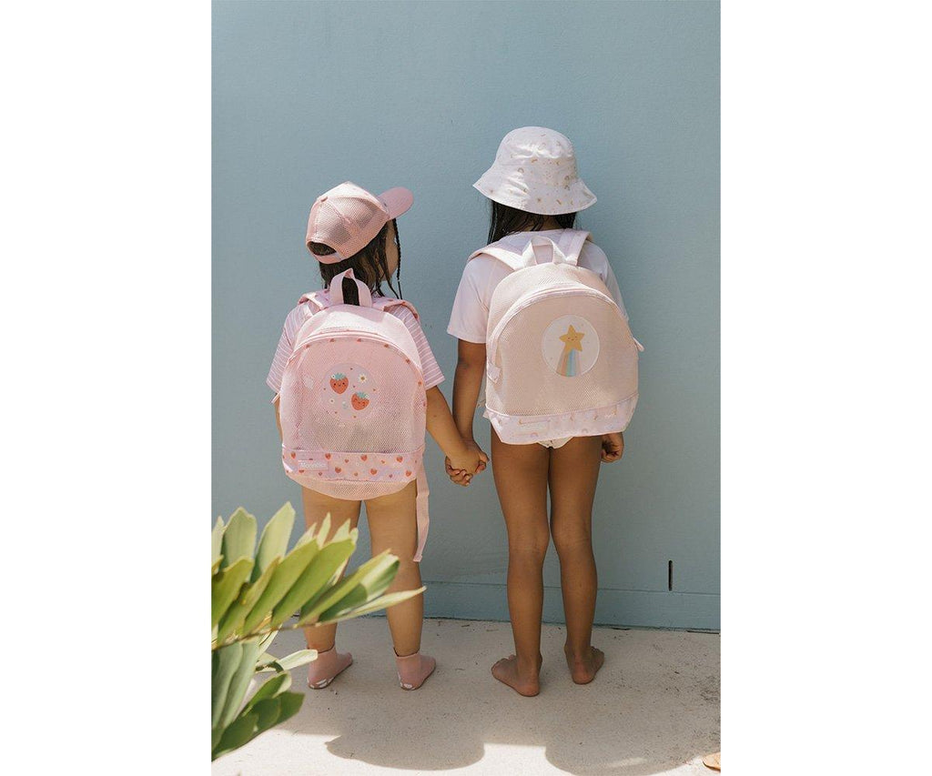 Duas crianças de costas, usando mochilas Monneka anti-areia (uma de morangos e outra de estrelas) junto a uma parede azul clara.