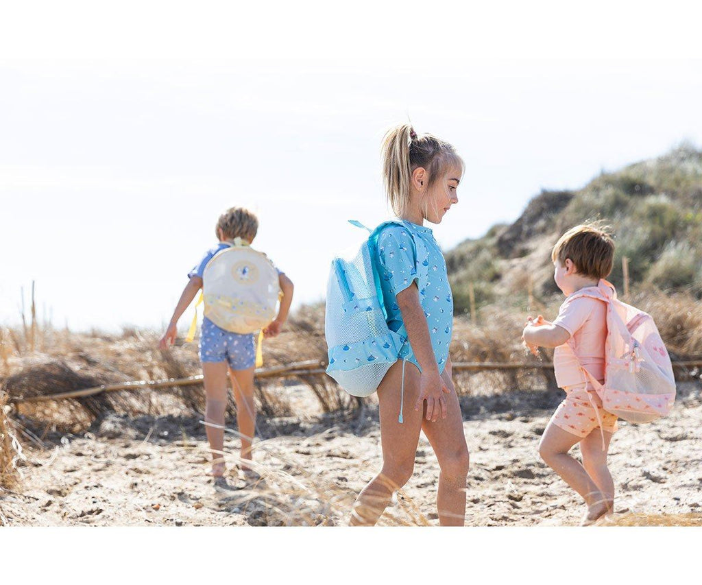 Crianças na praia a usar as mochilas Monneka anti-areia, demonstrando o uso prático em ambiente de areia.