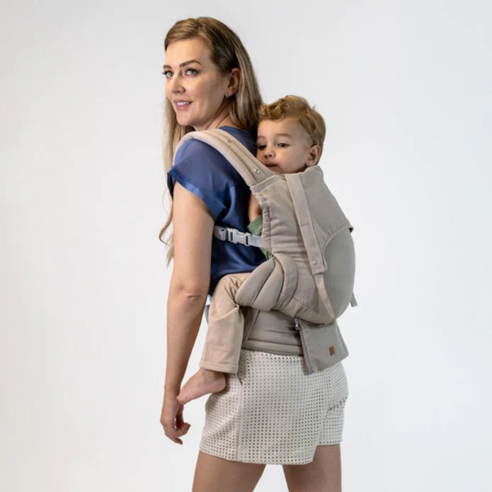 Mulher sorridente a usar a mochila Isara ELITE bege, transportando uma criança mais crescida nas costas, vista de lado.