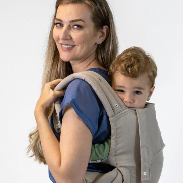 Mulher sorridente a usar a mochila Isara ELITE bege, transportando uma criança mais crescida na posição frontal, com a criança a olhar para a câmara.