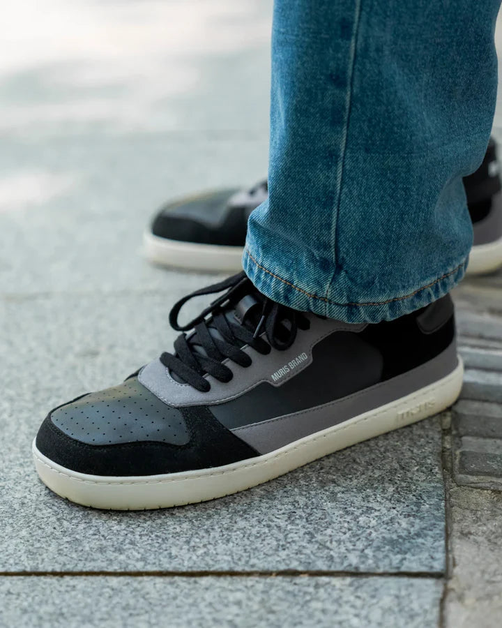 Detalhe da sapatilha Muris Majorca Black em uso, calçada com calças de ganga, mostrando o design barefoot e o fecho de velcro.