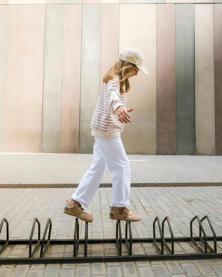 Criança a equilibrar-se em suportes de bicicleta, usando as sapatilhas Muris Petra Junior Bark Brown, demonstrando flexibilidade.