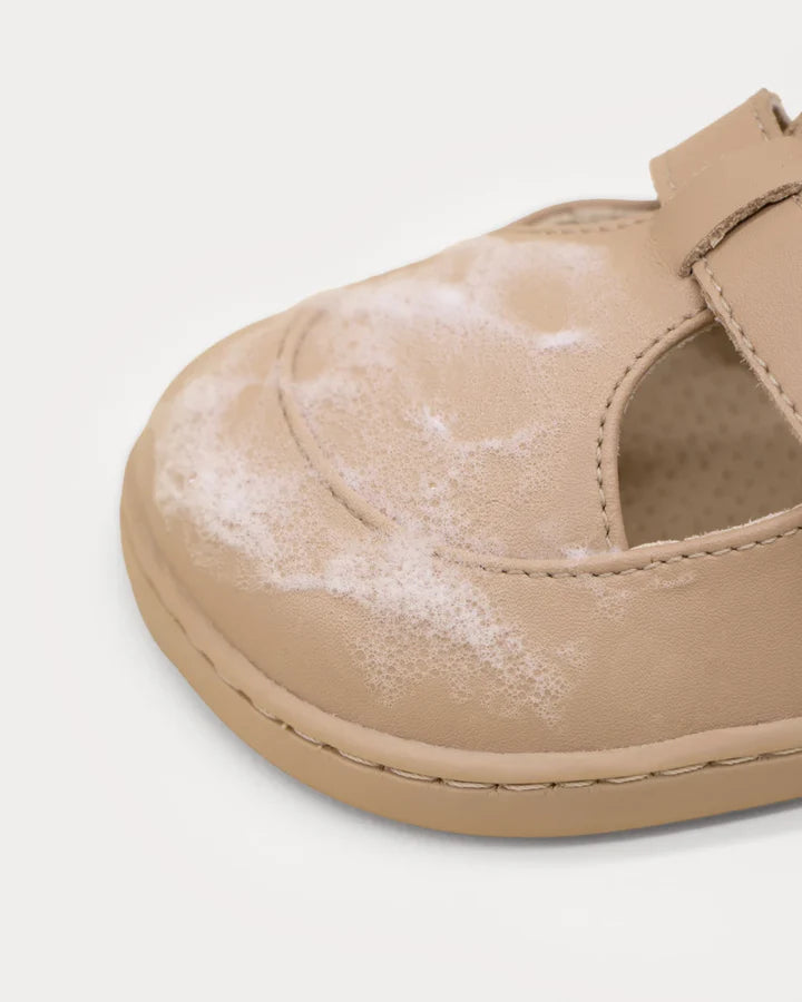 Detalhe de um sapato barefoot de bebé em tom bege a ser limpo com a espuma do kit Muris.