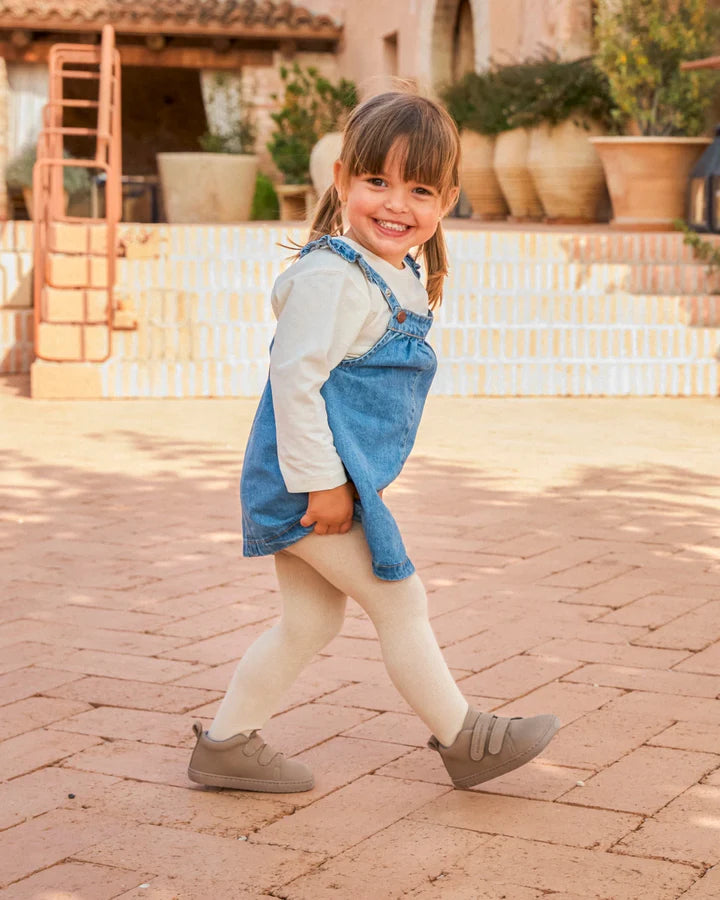 Menina sorrindo, usando as Muris Barefoot Bota Oslo Mini Elephant Gray com vestido de ganga e collants, num ambiente exterior soalheiro.