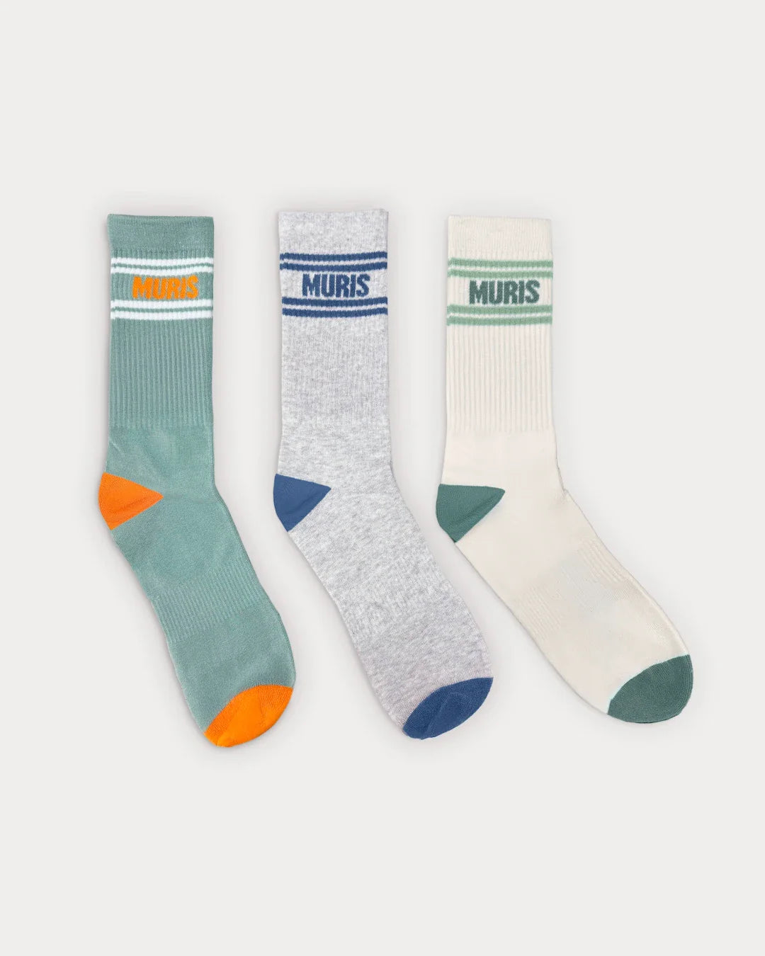 Três meias Muris Respeitadoras Homem de pé, em tons de azul-esverdeado, cinzento e branco, cada uma com riscas, logótipo "MURIS" e detalhes coloridos na ponta e calcanhar.