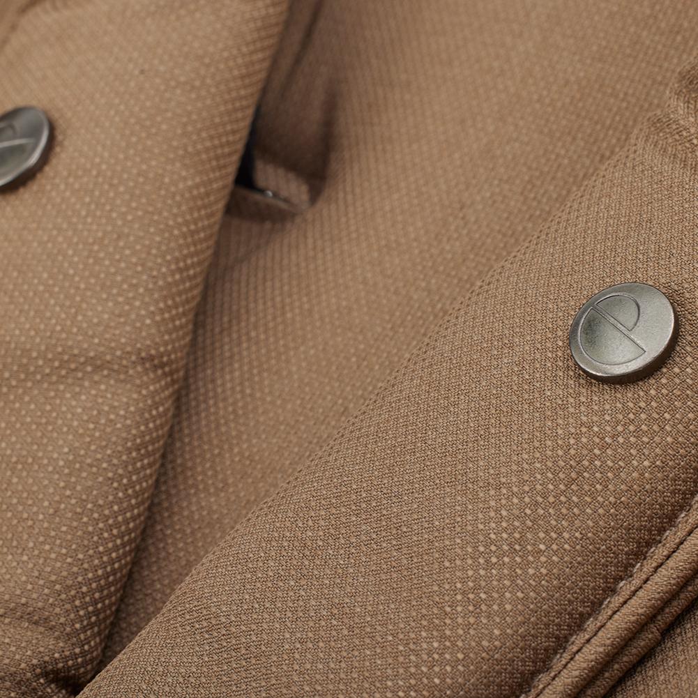 Detalhe macro do tecido castanho (Hazel) do carrinho Mutsy Flow, focando nos botões de pressão metálicos com o logótipo da marca.