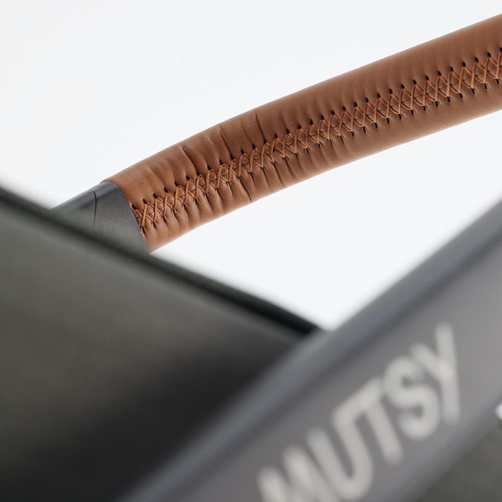 Close-up do guiador do carrinho Mutsy Flow, exibindo o acabamento em pele castanha com costura manual detalhada, foco na qualidade do material.