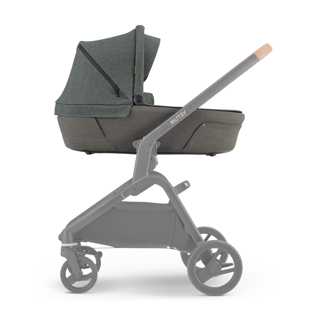 Alcofa Mutsy Flow em tom verde musgo (Urban Green) montada no chassis cinzento, vista lateral, com pega em pele castanha clara.