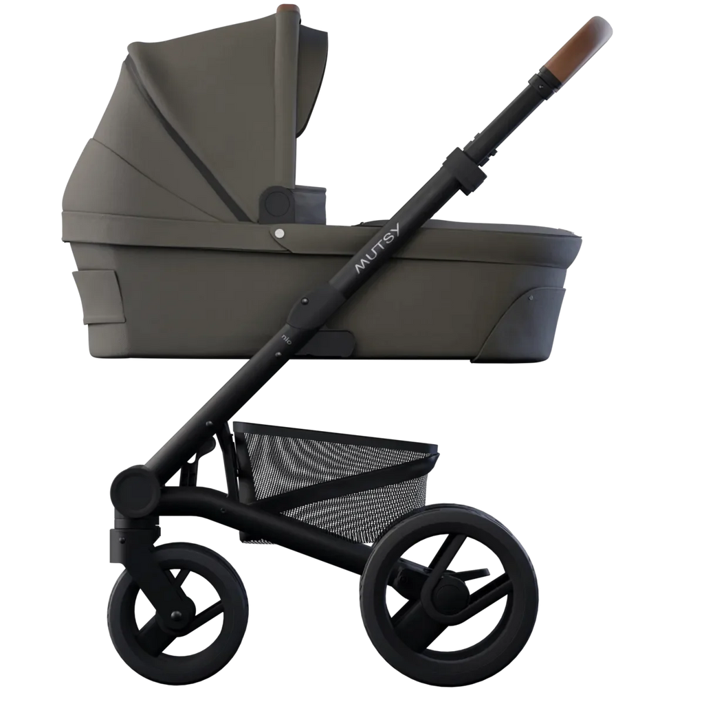 Carrinho Mutsy Nio com alcofa, perfil lateral, cor verde/castanha, guiador com detalhe em pele castanha clara e suspensão robusta.