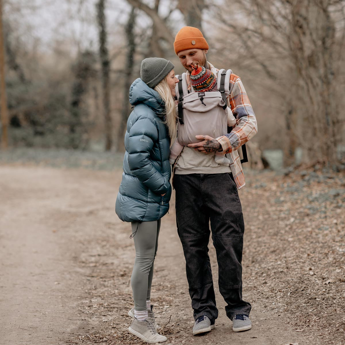 Casal a caminhar ao ar livre, ambos com casacos de inverno, transportando o bebé na Mochila Neobulle.