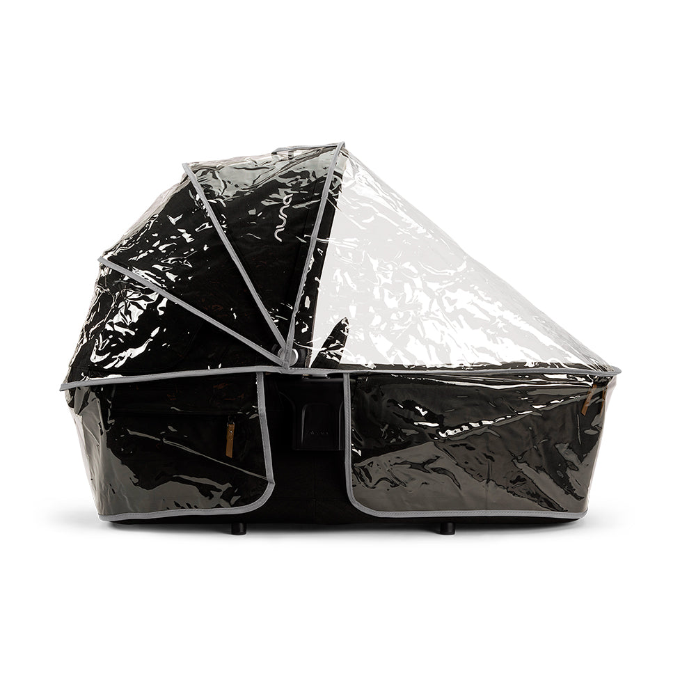 Alcofa Nuna LYTL preta coberta com capa de chuva transparente, protegendo contra intempéries.