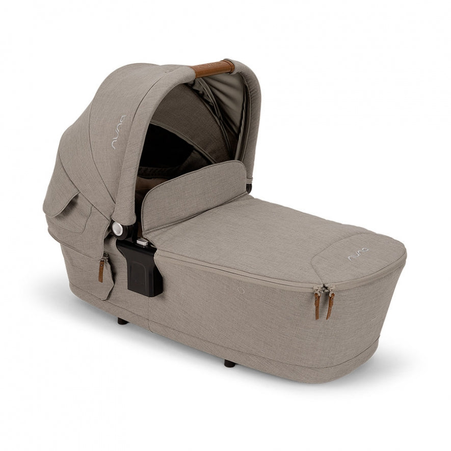 Alcofa Nuna MIXX NEXT em cor bege/castanho claro, vista em ângulo, mostrando detalhes de fechos e alça de transporte em couro.