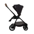 Carrinho de passeio Nuna TRIV NEXT preto, visto de lado, com capota estendida e alça em couro sintético castanho.