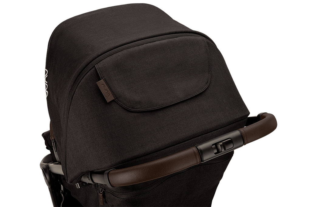 Detalhe em close-up do topo do carrinho Nuna TRVL LX preto, focando na capota extensível e no apoio de braço com acabamento em pele castanha.