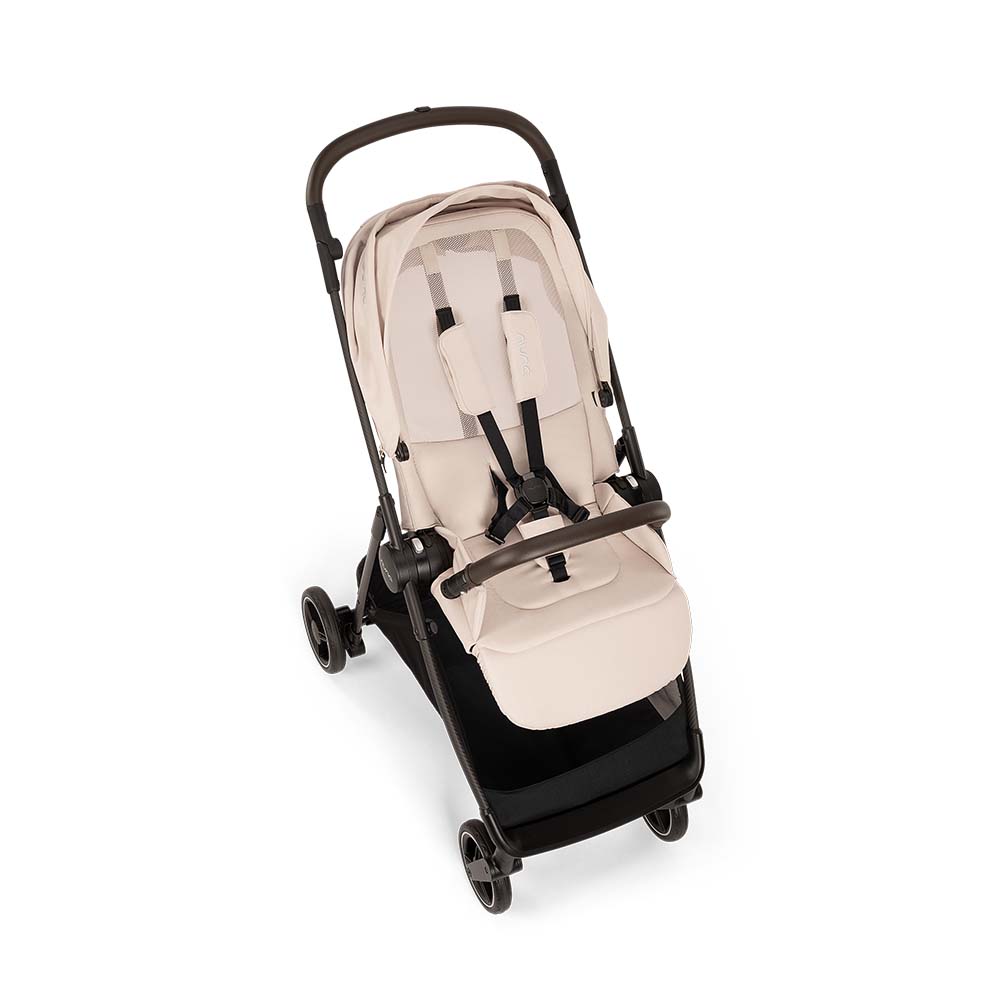Vista superior do carrinho Nuna IXXA NEXT bege, mostrando o assento com arnês de 5 pontos e barra de segurança.