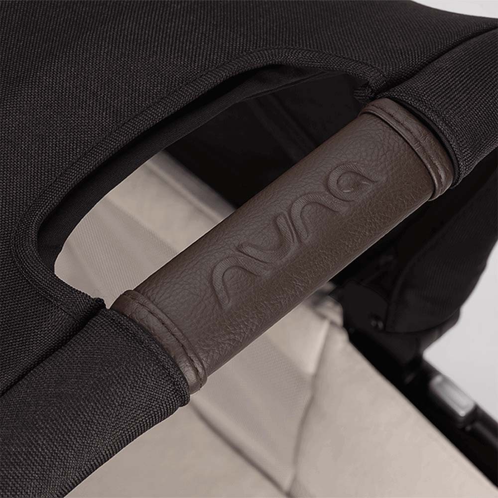 Detalhe do manípulo de empurrar do carrinho Nuna com capa em pele sintética castanha escura e logótipo NUNA gravado.