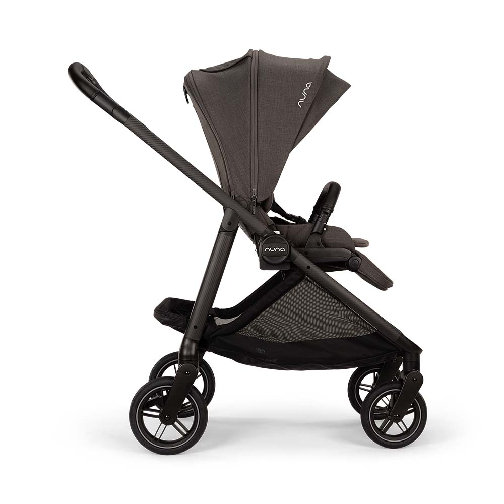 Carrinho Nuna SWIV 360 cor Granite, visto de lado, com assento virado para o condutor e guiador ajustável. Estrutura escura e cesto de arrumação em malha.