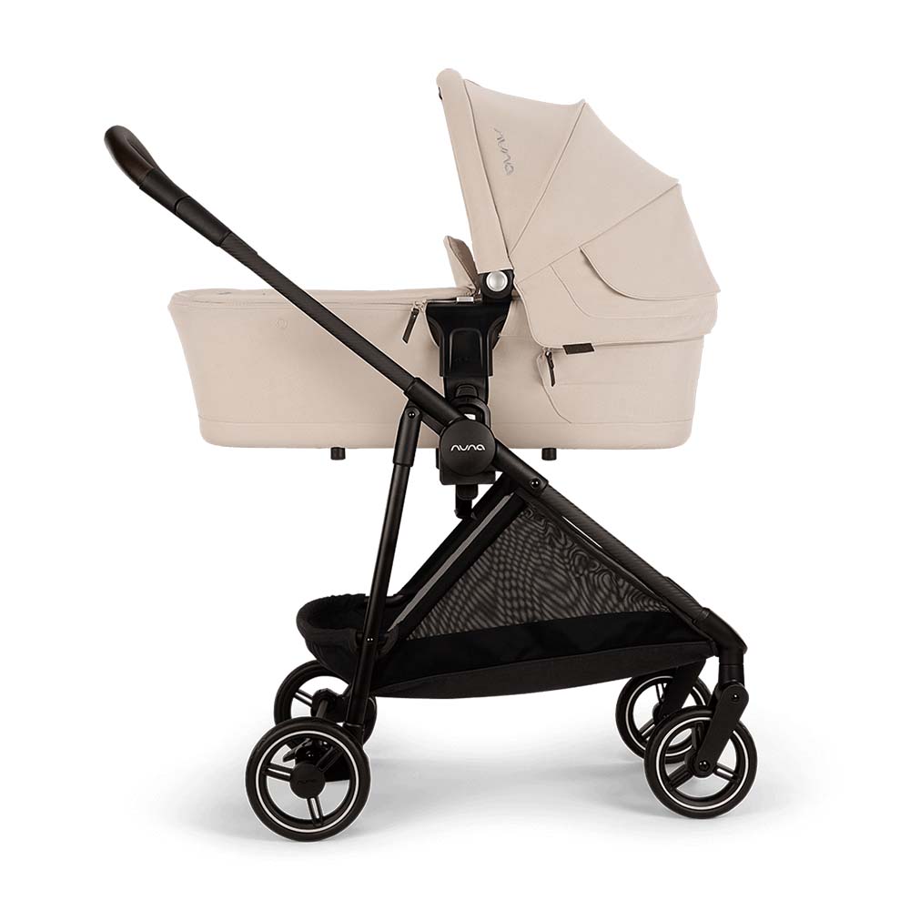 Carrinho Nuna IXXA NEXT com alcofa acoplada, visto de lado, mostrando a capacidade de configuração para recém-nascidos. Cor bege com detalhes pretos.