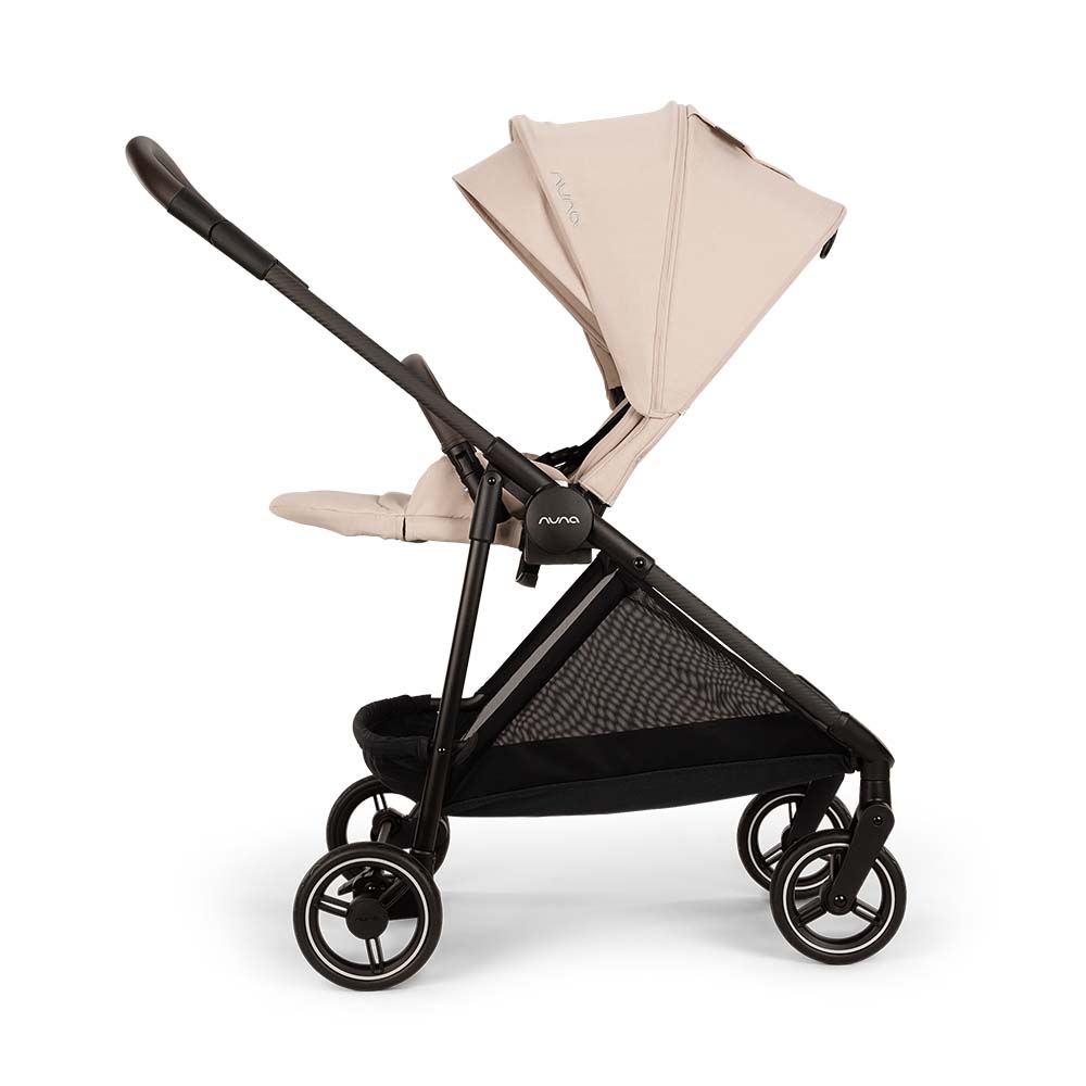 Carrinho de passeio Nuna IXXA NEXT em cor bege claro, visto de lado, com assento virado para a frente e capota estendida. Estrutura preta e cesto de arrumação em rede.