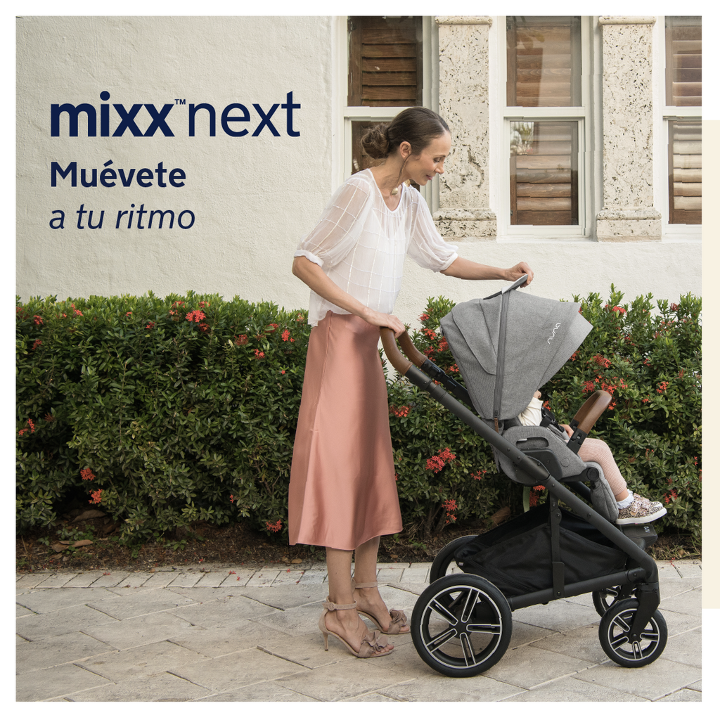 Mãe ajusta a capota do carrinho Nuna MIXX NEXT cinzento, com criança sentada, em frente a uma parede branca e vegetação.