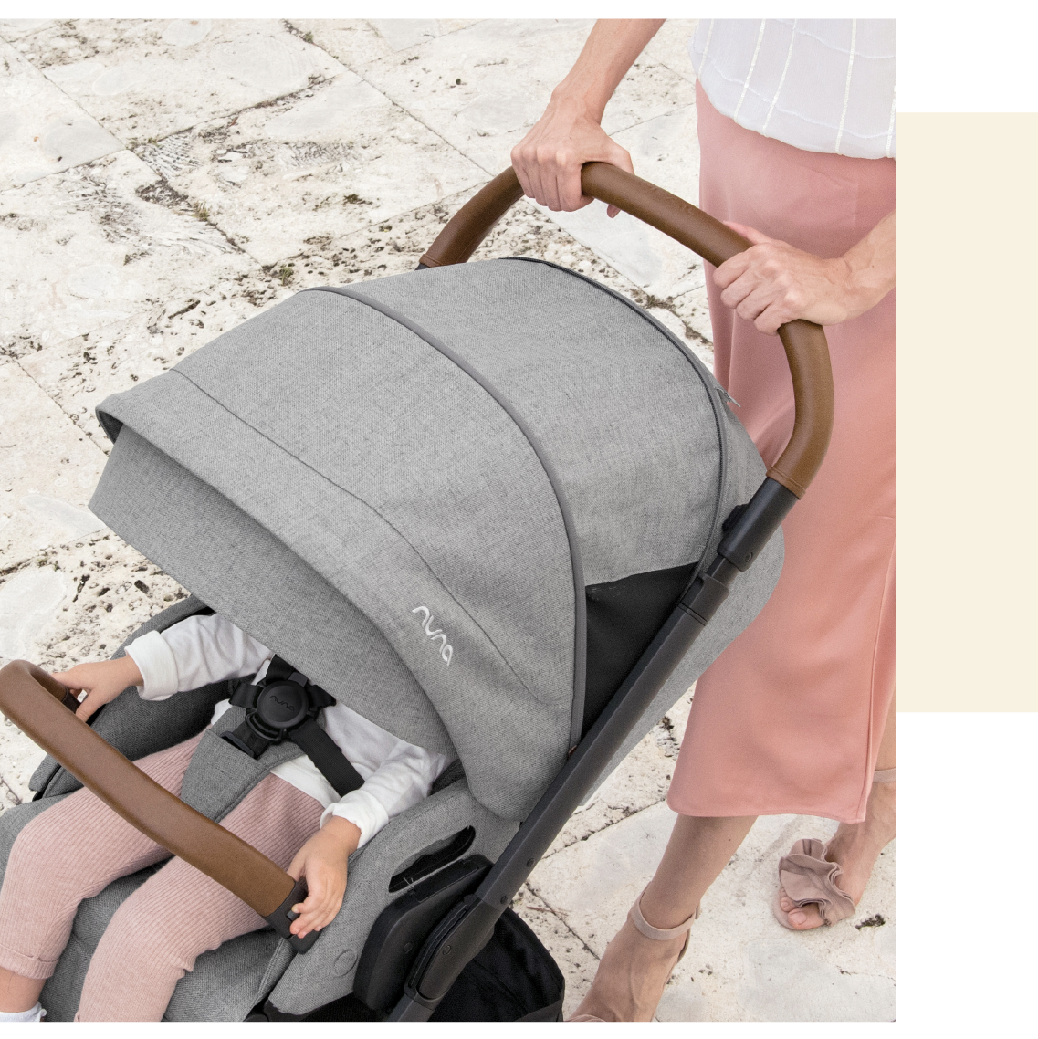 Detalhe superior do carrinho Nuna MIXX NEXT cinzento, mostrando o arnês, pega em pele castanha e criança a segurar a barra frontal.