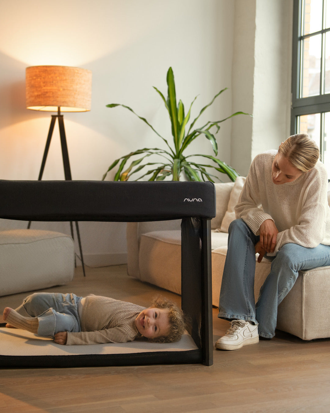 Bebé deitado na cama de viagem Nuna PAAL, mostrando o conforto e a versatilidade do produto em diferentes ambientes.