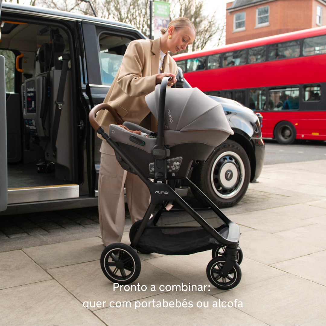 Mulher a acoplar um porta-bebés Nuna ao chassis do carrinho TRIV NEXT em ambiente urbano, ilustrando a funcionalidade de sistema de viagem.