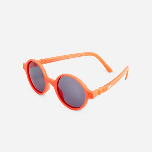 Óculos de sol infantis Ki ET LA RoZZ, modelo redondo, cor laranja vivo, em fundo cinzento claro.