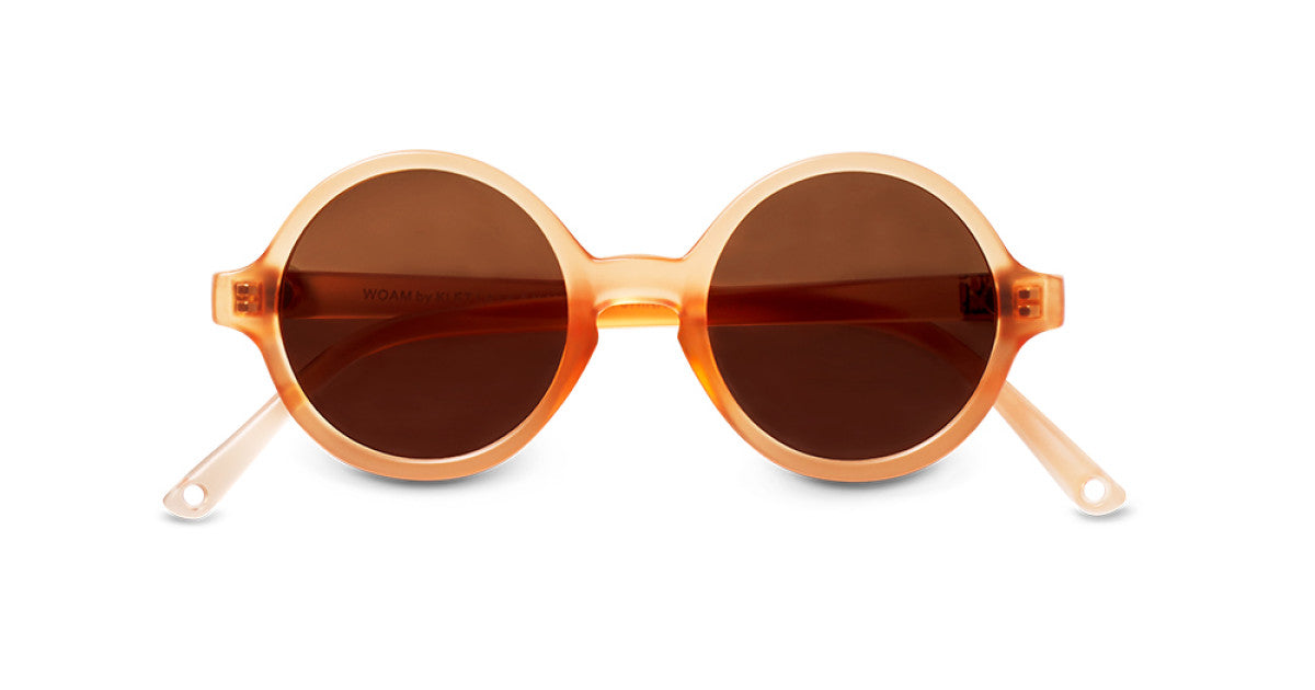 Primeiro plano de óculos de sol infantis Ki ET LA WOAM, modelo redondo, com armação translúcida cor mostarda e lentes castanhas escuras.
