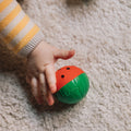 Mão de bebé a segurar uma bola sensorial Oli&Carol com forma de melancia.