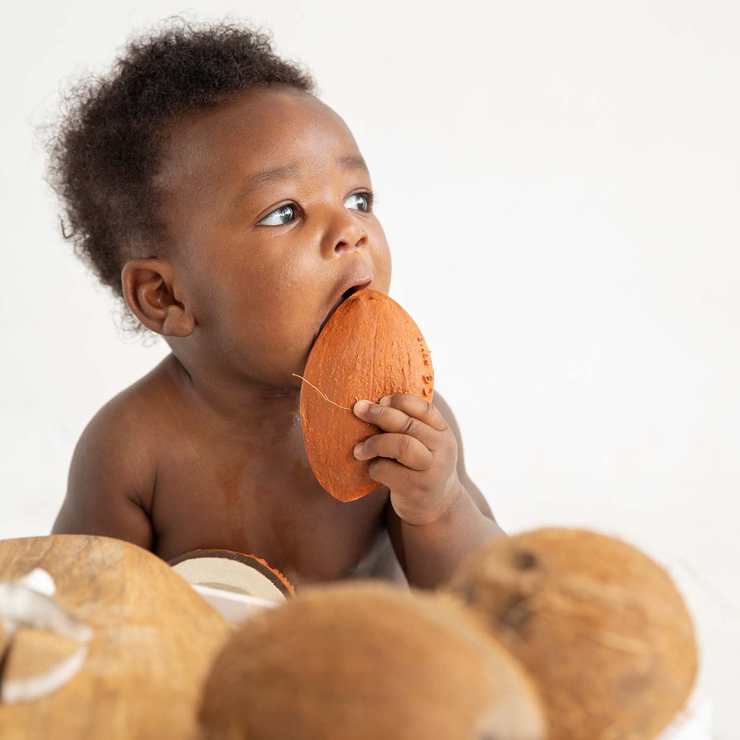 Bebê afro-americano brincando com o mordedor Coco the Coconut da Oli & Carol, destacando a sua textura suave e segura.