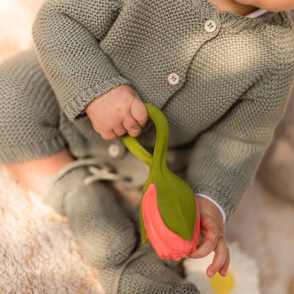 Mãos de bebê segurando o mordedor Oli & Carol Theo a Tulipa, mostrando o seu design ergonômico.