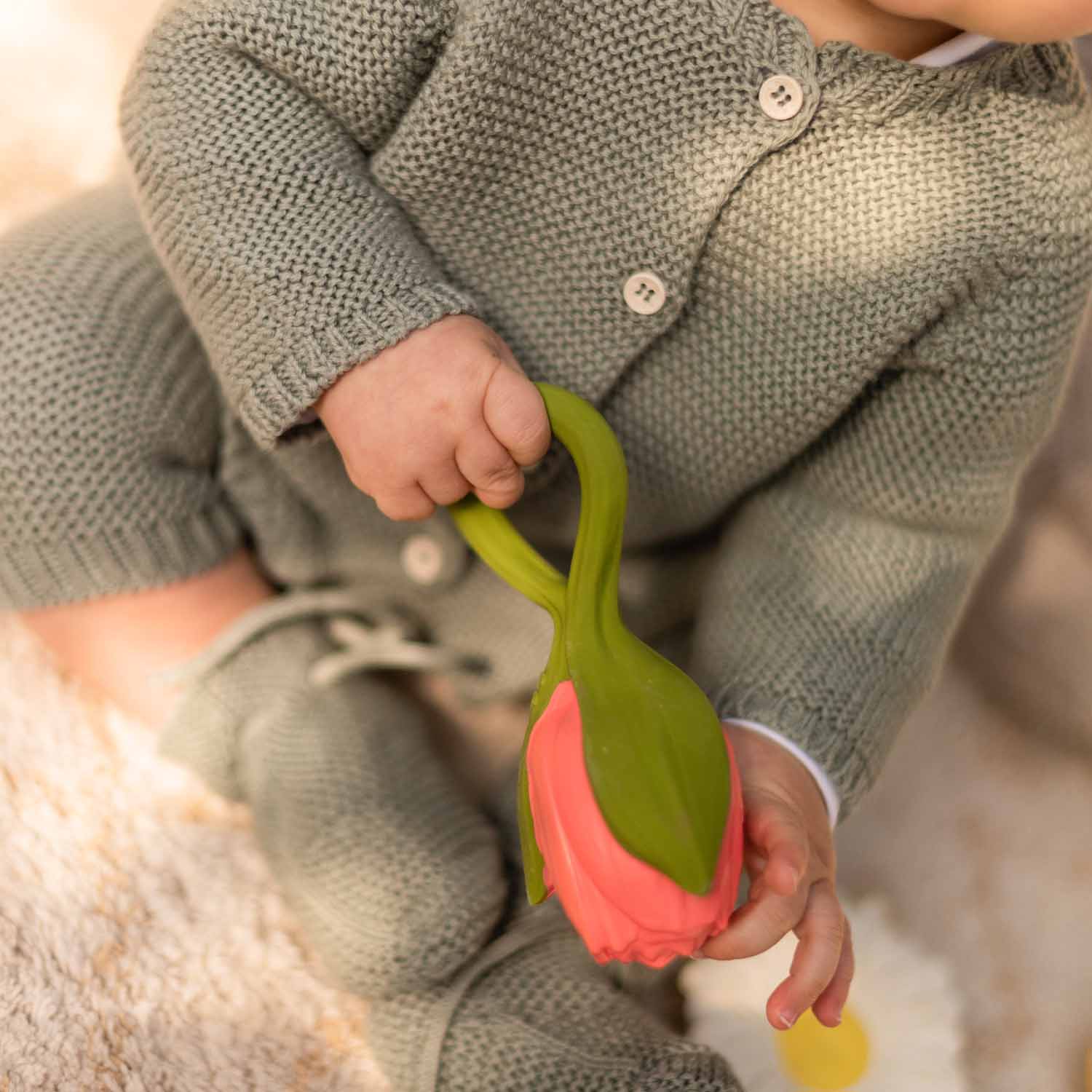 Mãos de bebê segurando o mordedor Oli & Carol Theo a Tulipa, mostrando o seu design ergonômico.