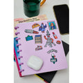 Caderno de argolas lilás personalizado com vários autocolantes OMY de Paris, junto a um telemóvel e auscultadores brancos.