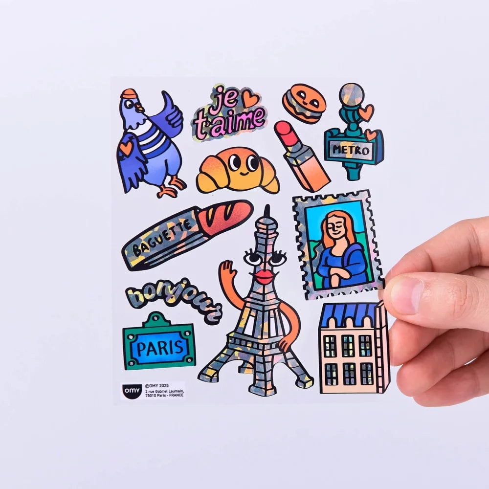 Mão a segurar uma folha de autocolantes OMY com desenhos de Paris, como pombo, baguette, batom e a Mona Lisa estilizada.