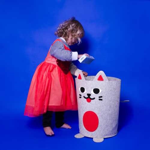 Criança pequena a colocar um objeto no cesto de arrumação OMY em forma de gato, com fundo azul vibrante.