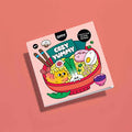Capa do caderno de colorir OMY "Cozy Yummy" com ilustração de um prato de ramen colorido, sobre fundo rosa.