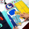 Close-up do OMY Livro Play Kit Montessori mostrando a atividade de colocar as peças de roupa no urso de peluche.