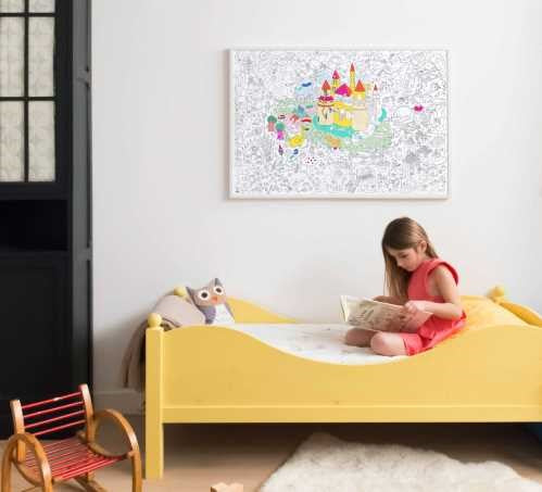 Uma menina sentada numa cama amarela, a colorir o póster gigante OMY Magic.